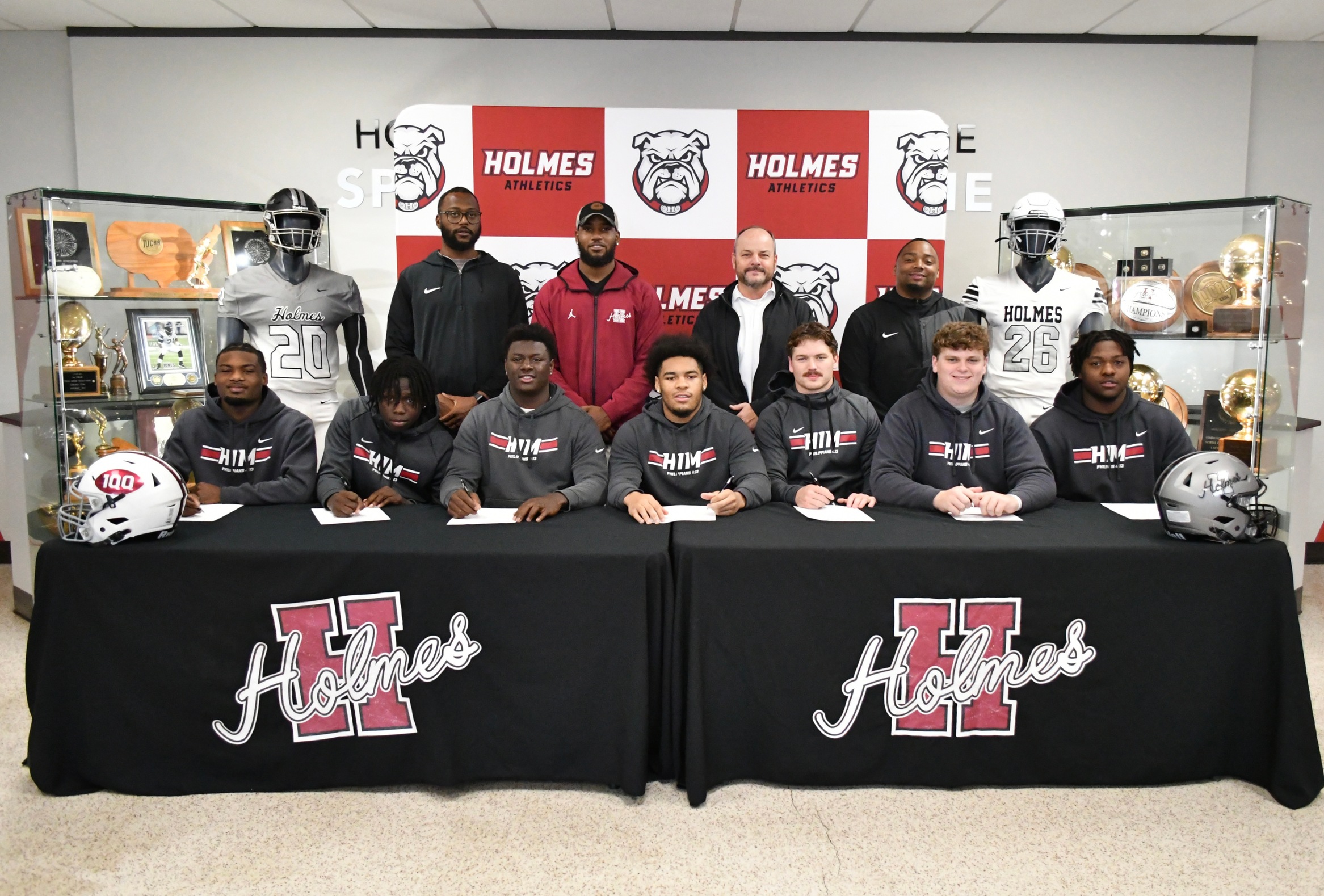 Seven Holmes CC football players signed with four-year schools today. Pictured (front, l-r) P.J. Pace, Jeremy Atkins, Lionel Williams, E.J. Segrest, Cayden Burger, Jon Stephens and Jaylin Rogers; and (back row, l-r) Assistant Head Coach/LB Coach/Defensive Coordinator C.J. Johnson, QB Coach/Pass Game Coordinator De'Andre Johnson, Head Coach Marcus Wood and Offensive Coordinator/WR Coach Kam Myers.